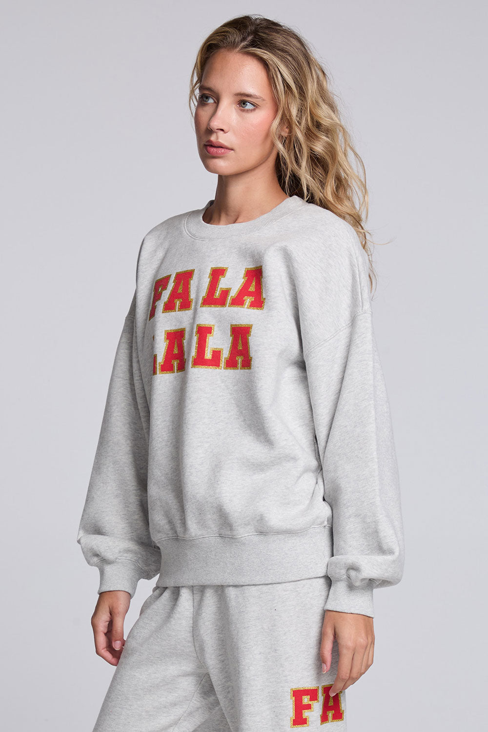 Model wearing Chaser's Fa La La La Pullover in Heather Grey with oversized red Fa La La La lettering, angled view