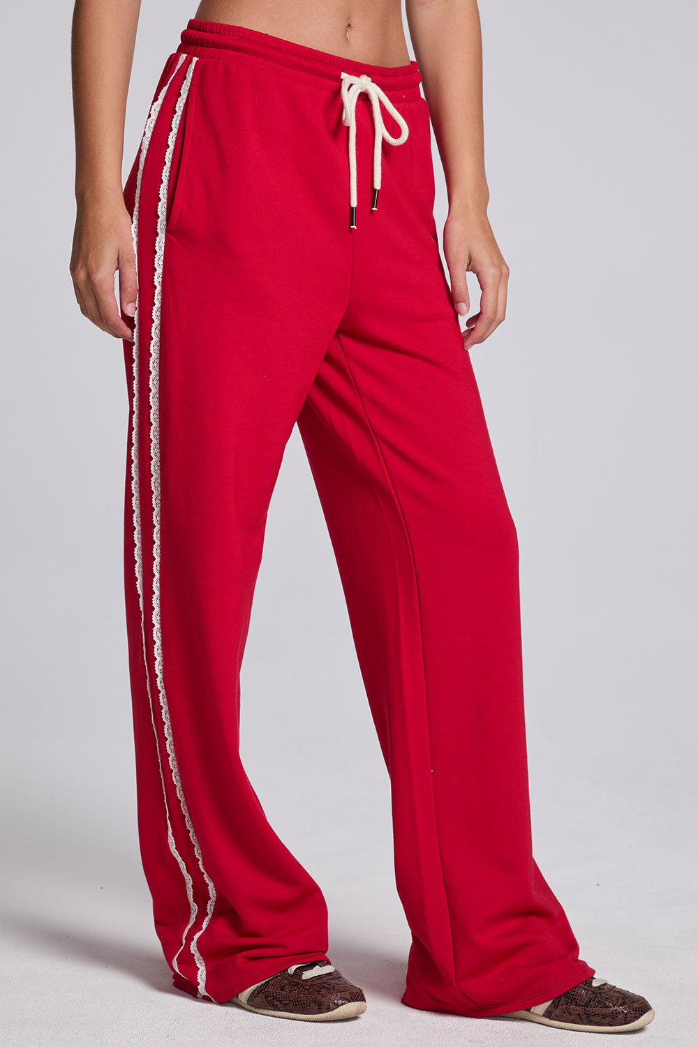 Model wearing Chaser's Cherry Bomb Delilah Track Pants in Cherry Bomb red wide-leg track pants with contrast side stripes, angled view