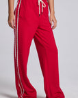 Model wearing Chaser's Cherry Bomb Delilah Track Pants in Cherry Bomb red wide-leg track pants with contrast side stripes, angled view