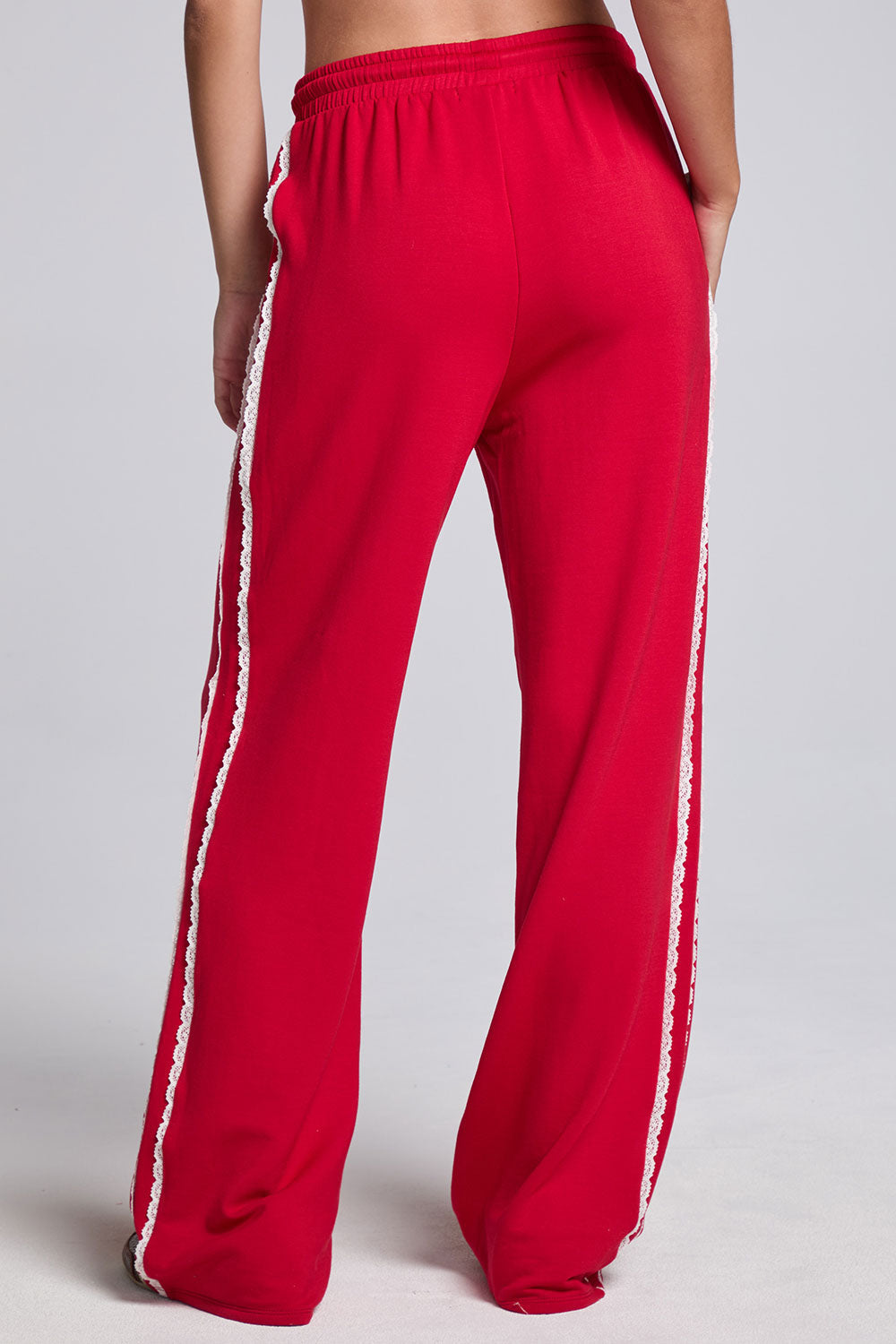 Model wearing Chaser's Cherry Bomb Delilah Track Pants in Cherry Bomb red wide-leg track pants with contrast side stripes, back view