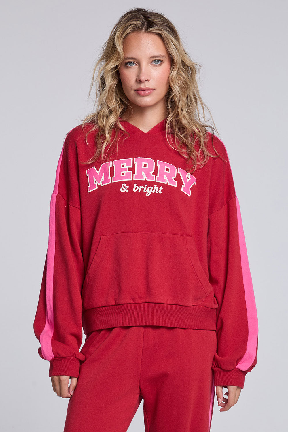 Model wearing Chaser's Merry and Bright Hoodie in Cranberry Velvet with varsity-style Merry and Bright artwork, front view