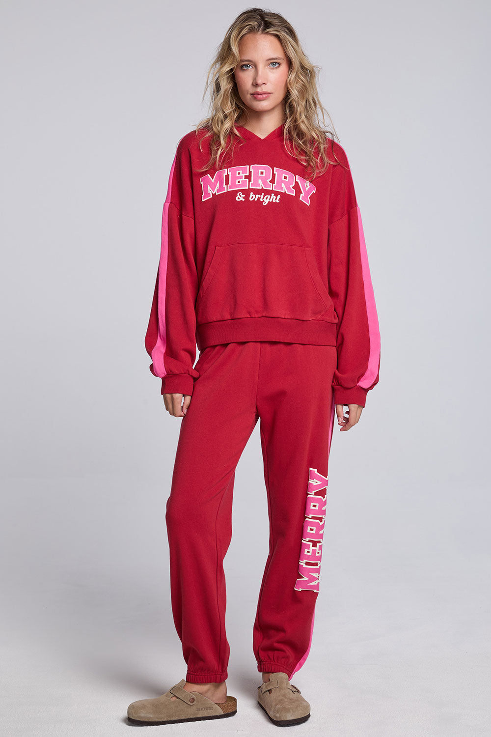 Model wearing Chaser's Merry and Bright Hoodie and matching Merry and Bright Jogger in Cranberry Velvet with holiday lettering, full-body view