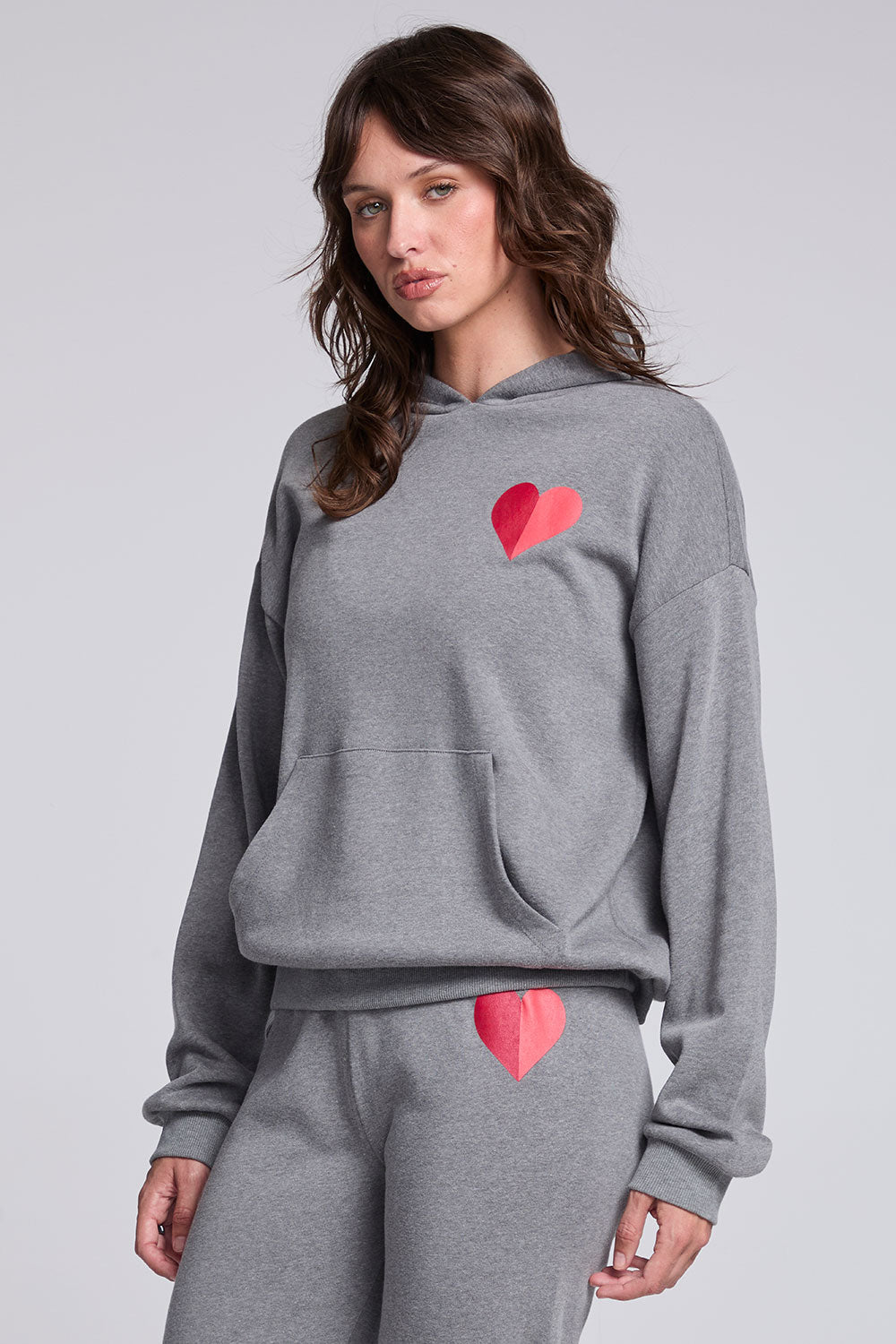 Model wearing Chaser's Dual Tone Heart Hoodie in Streaky with a single red heart, angled view