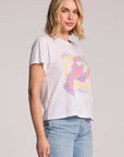 Side angle view of a woman wearing the Chaser  Catch Of The Day Tee on a neutral background with her hands down 