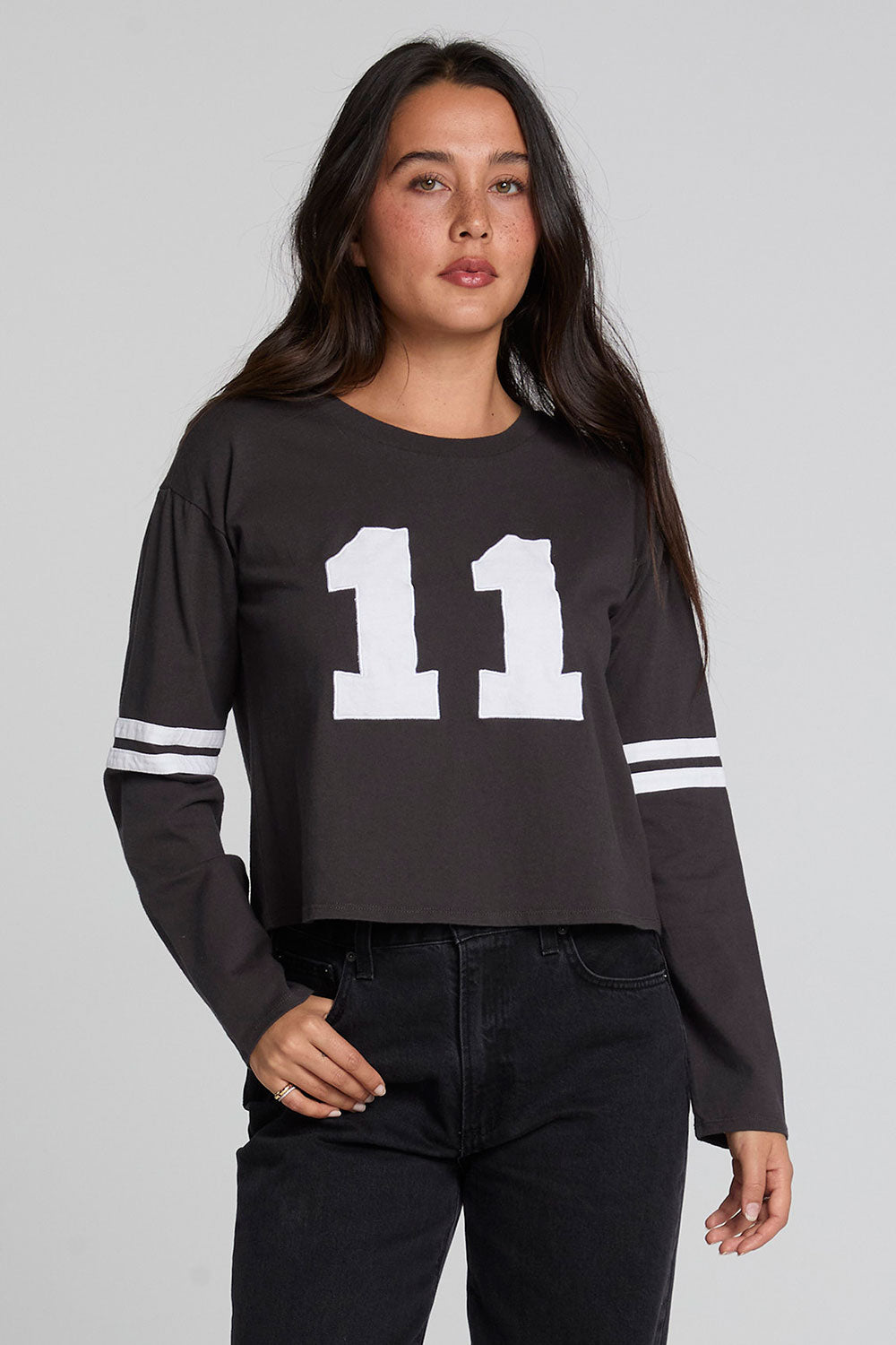 Front view of a woman wearing the Chaser 11 Long Sleeve and black jeans on a neutral background with thumb in pocket