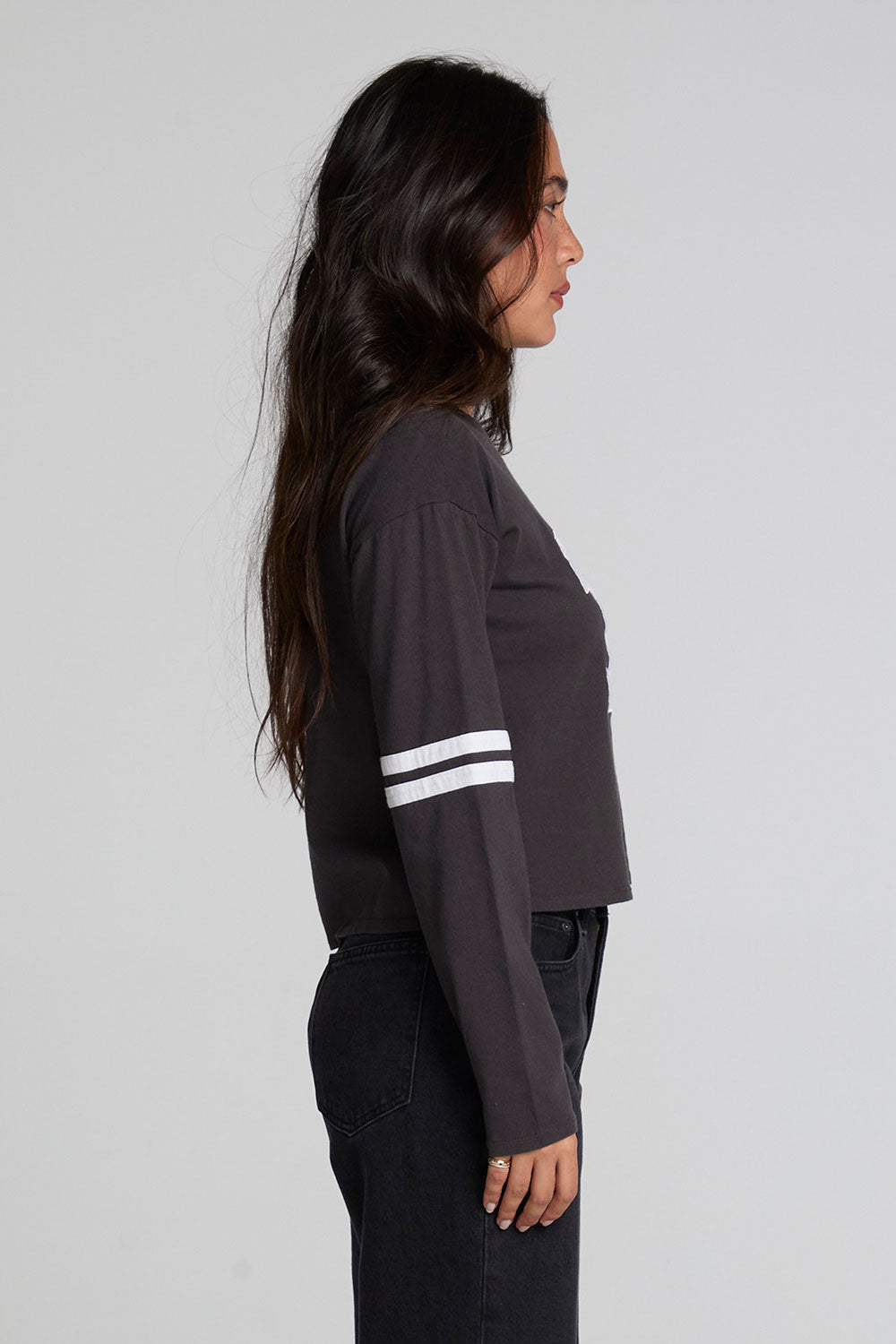 Side view of a woman wearing the Chaser 11 Long Sleeve and black jeans on a neutral background