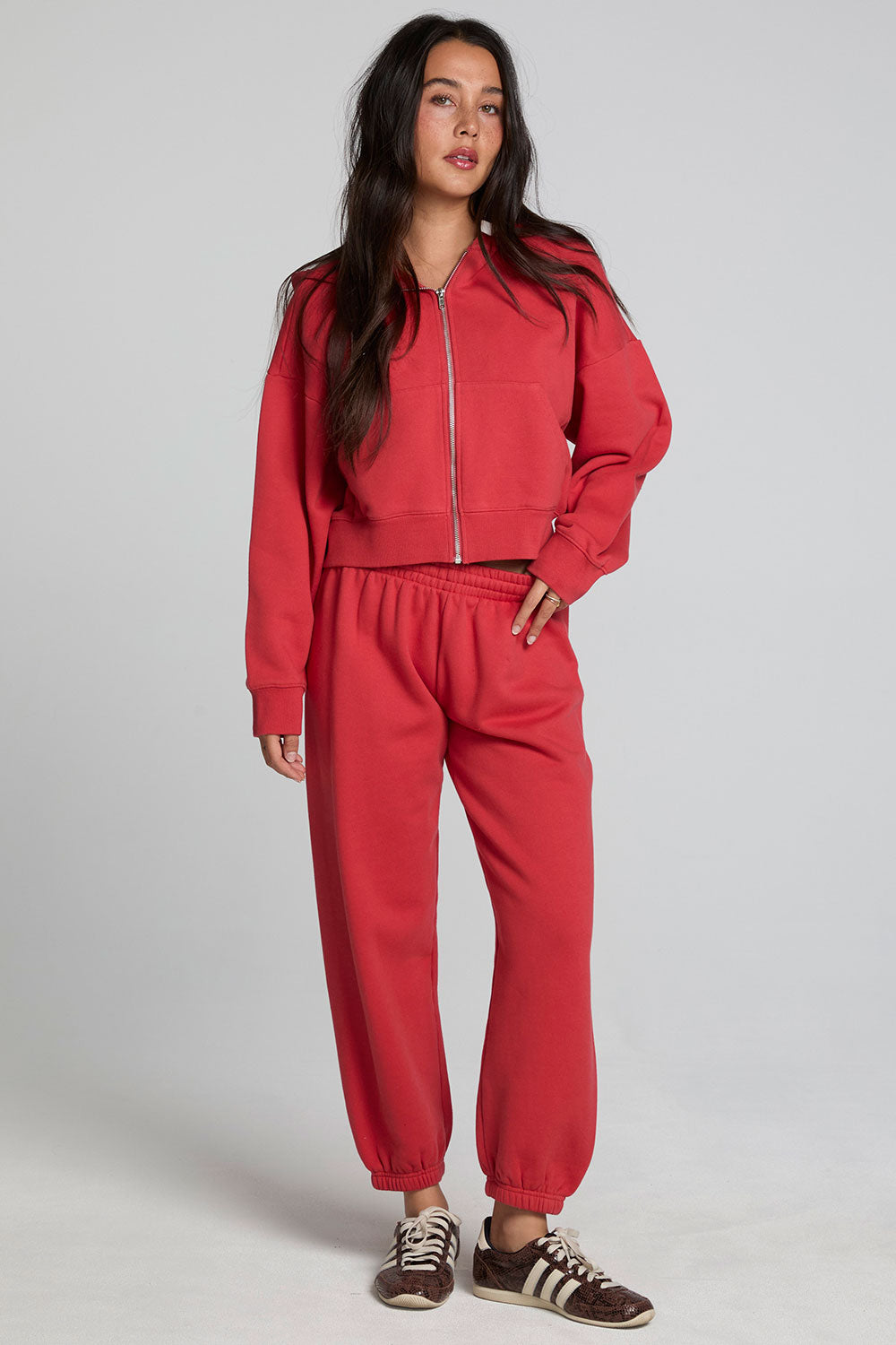 Full body front view of a woman wearing the Chaser Abilene Dry Red Zip Up on a neutral background with matching red pants