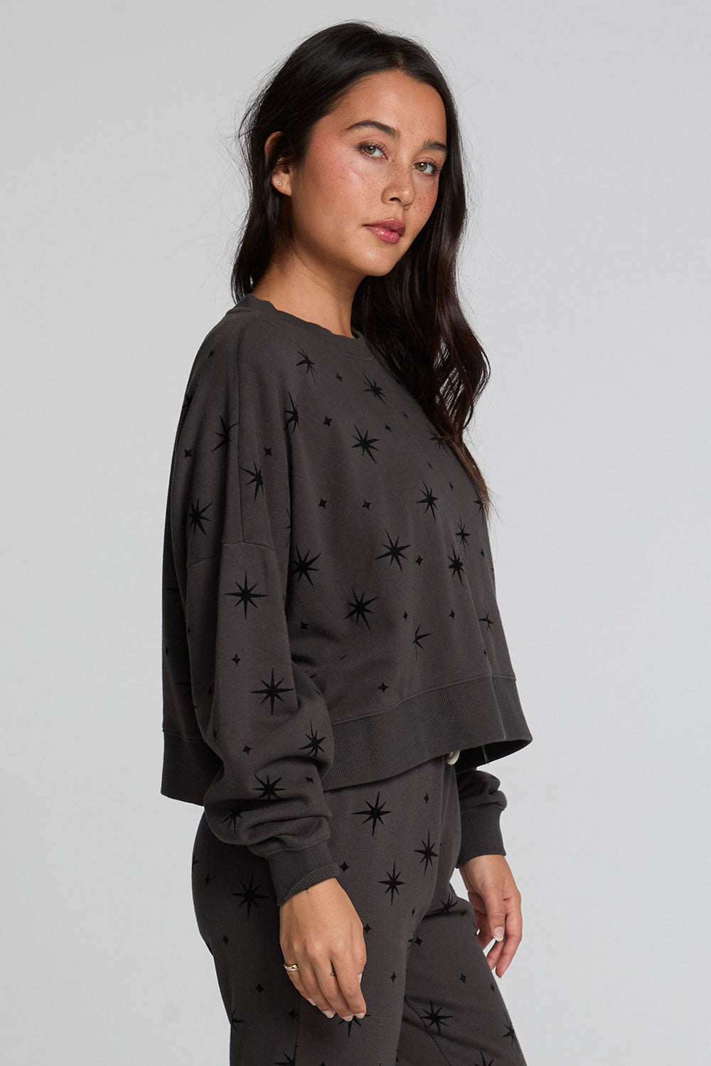 Side view of a woman wearing the Chaser Chaser Allover Mini Stars Long Sleeve and matching black pants on a neutral background