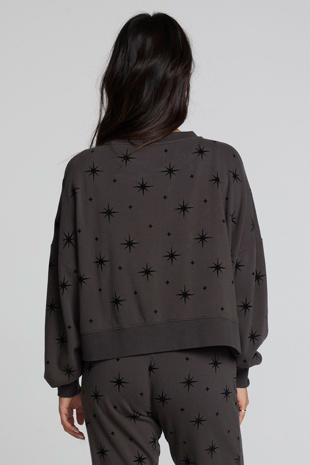 Back view of a woman wearing the Chaser Chaser Allover Mini Stars Long Sleeve and matching pants on a neutral background