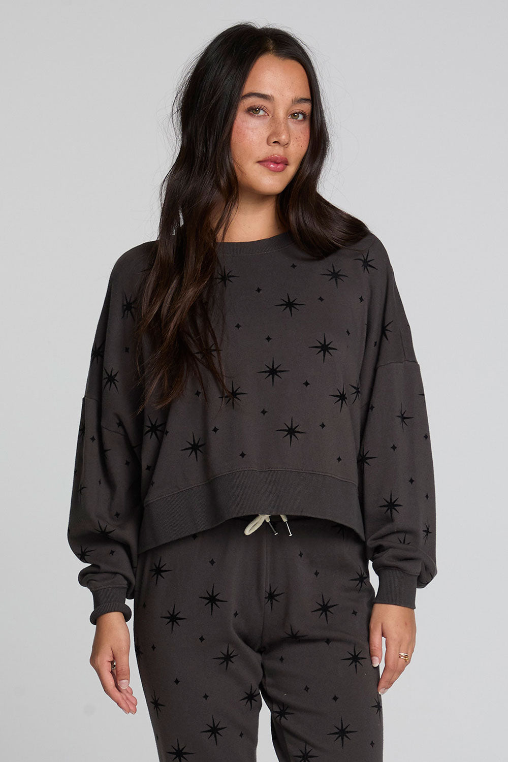 Back view of a woman wearing the Chaser Chaser Allover Mini Stars Long Sleeve and matching pants on a neutral background with arms lowered