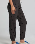 Side view of a woman wearing the Chaser  Allover Mini Stars Pants on a neutral background with hands at sides