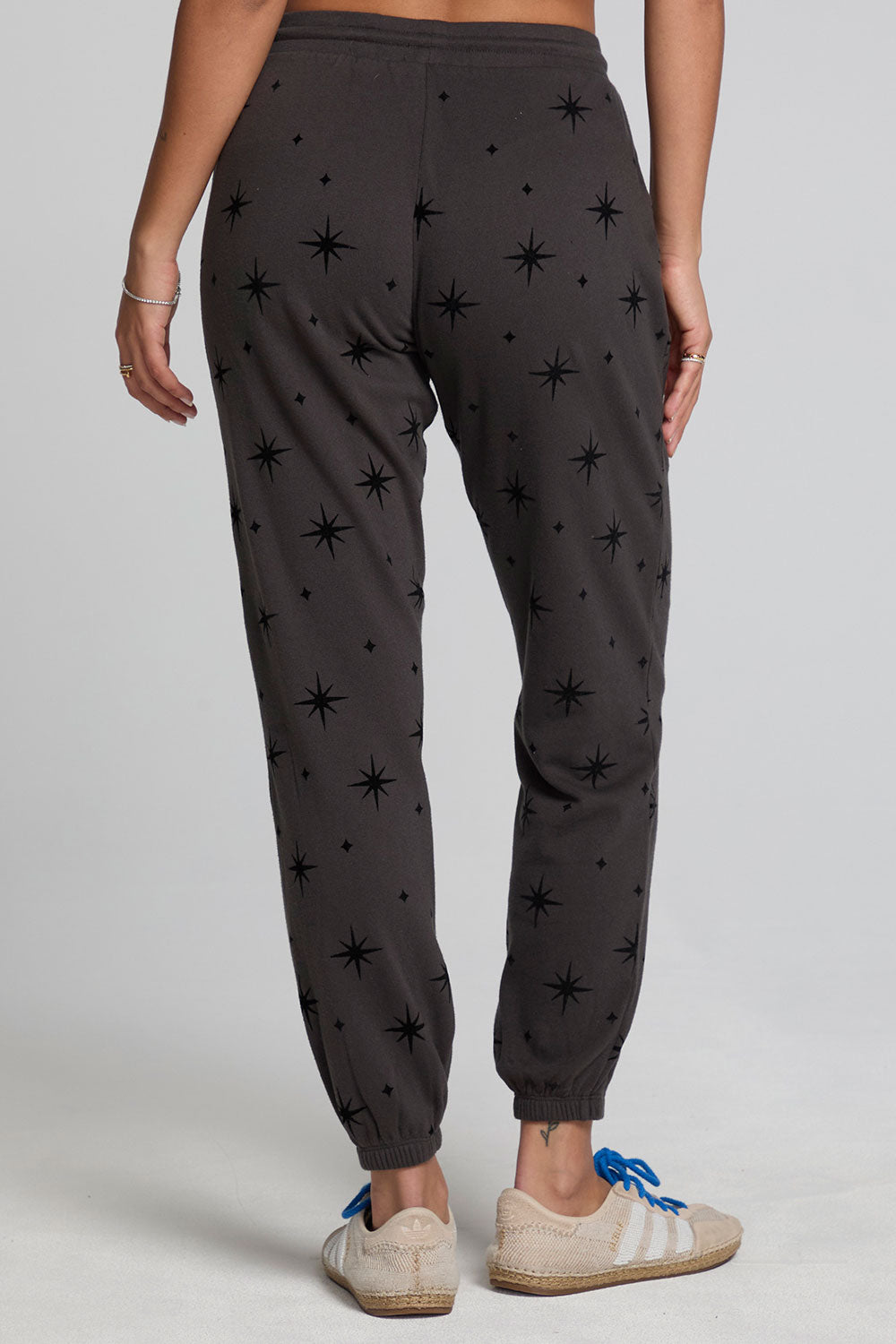Back view of a woman wearing the Chaser  Allover Mini Stars Pants on a neutral background