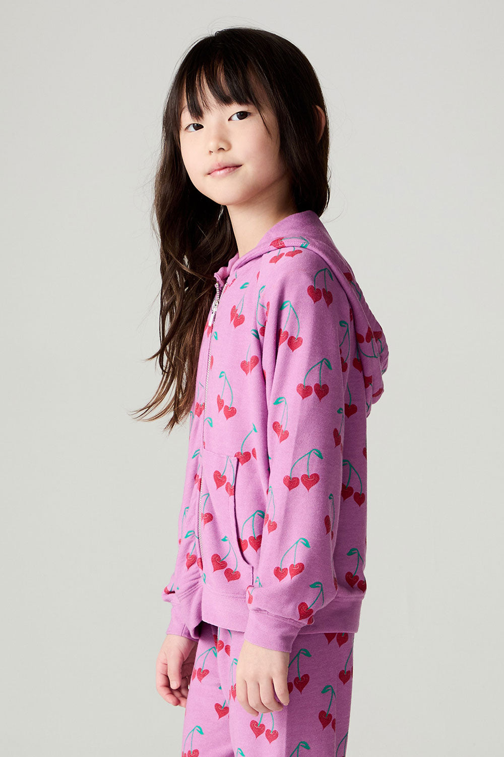 Side view of a girl wearing the Chaser Allover Sweethearts Girls Hoodie on a neutral background with matching pants