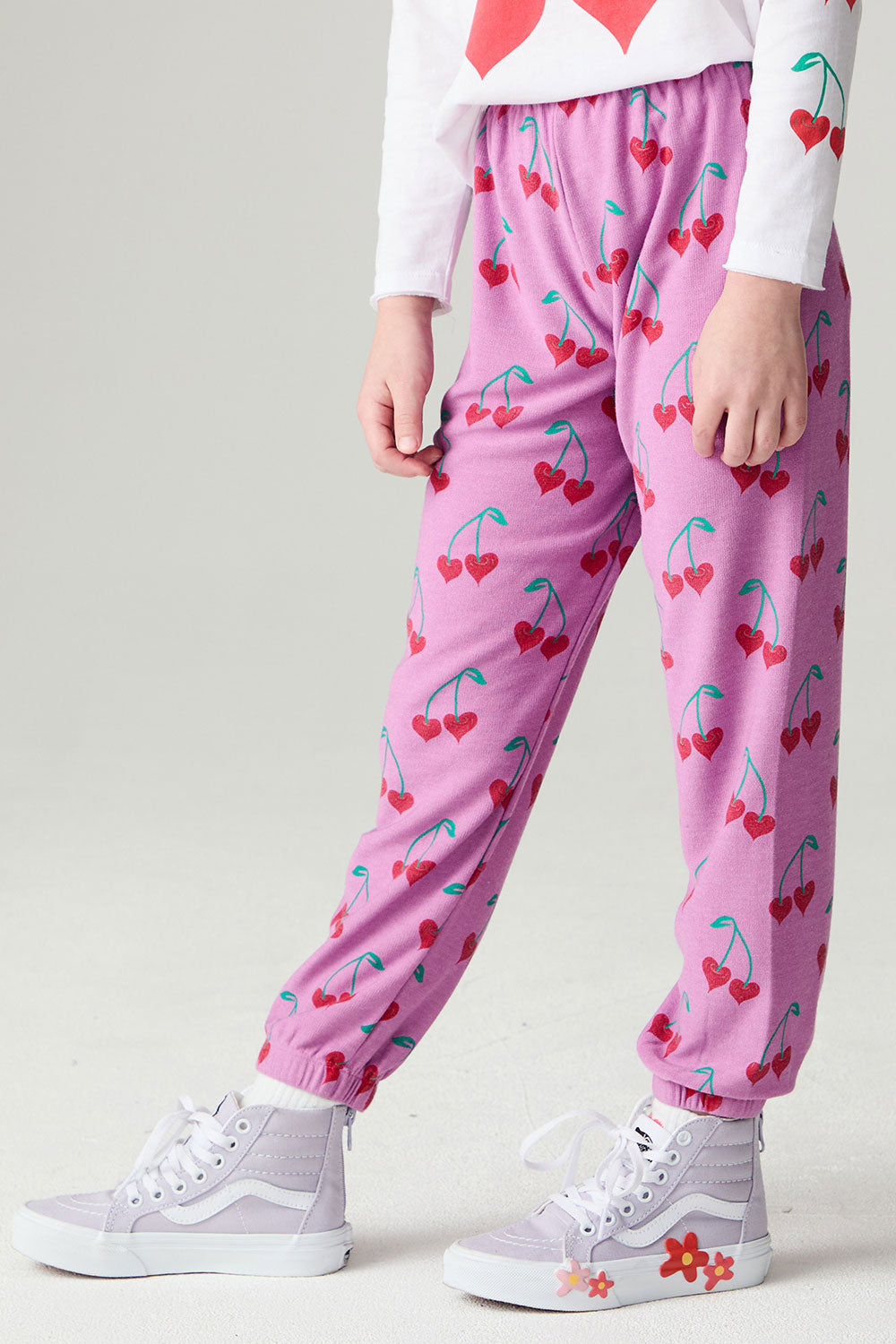 Side angle view of a girl wearing the Chaser Allover Sweethearts Girls Jogger on a neutral background with sneakers