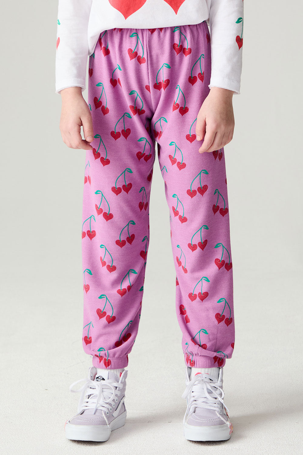 Front view of a girl wearing the Chaser Allover Sweethearts Girls Jogger on a neutral background with sneakers and shirt