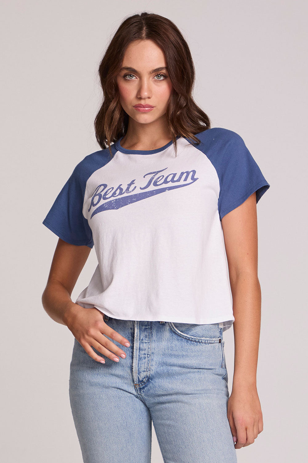 Front view of a woman wearing the Chaser Athletics Club Tee on a neutral background with blue jeans and hand in pocket