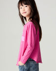 Side view of a girl wearing the Chaser Best Sister Girls Tee on a neutral background and blue jeans