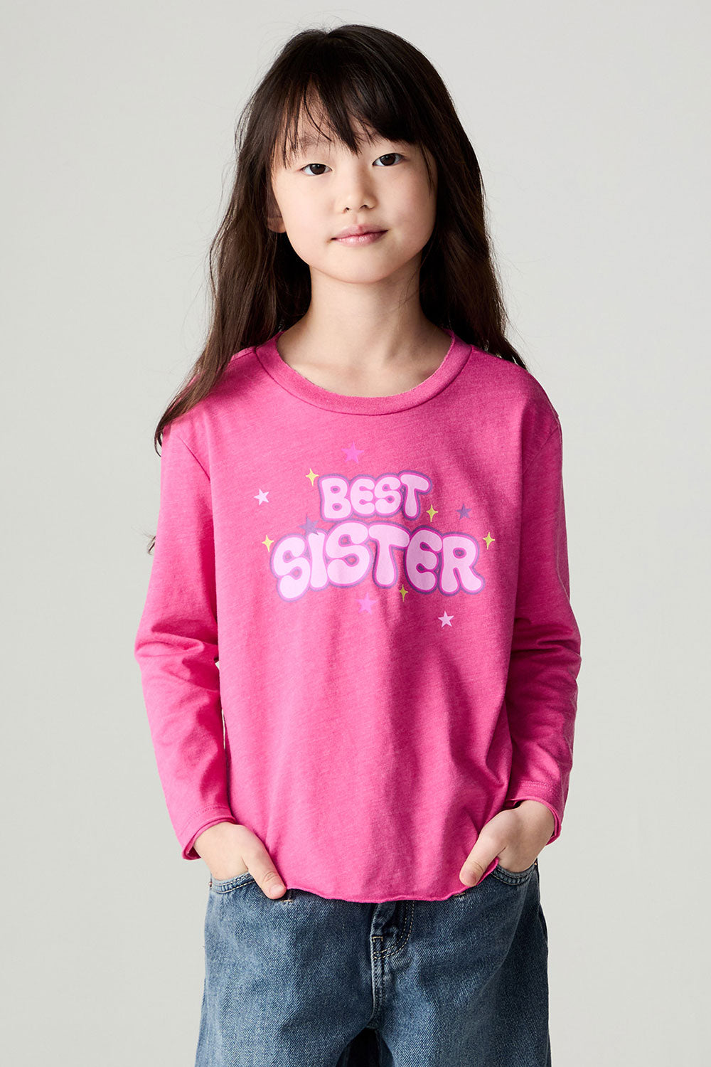 Front facing view of a girl wearing the Chaser Best Sister Girls Tee on a neutral background and baggy jeans