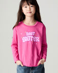 Front facing view of a girl wearing the Chaser Best Sister Girls Tee on a neutral background and baggy jeans
