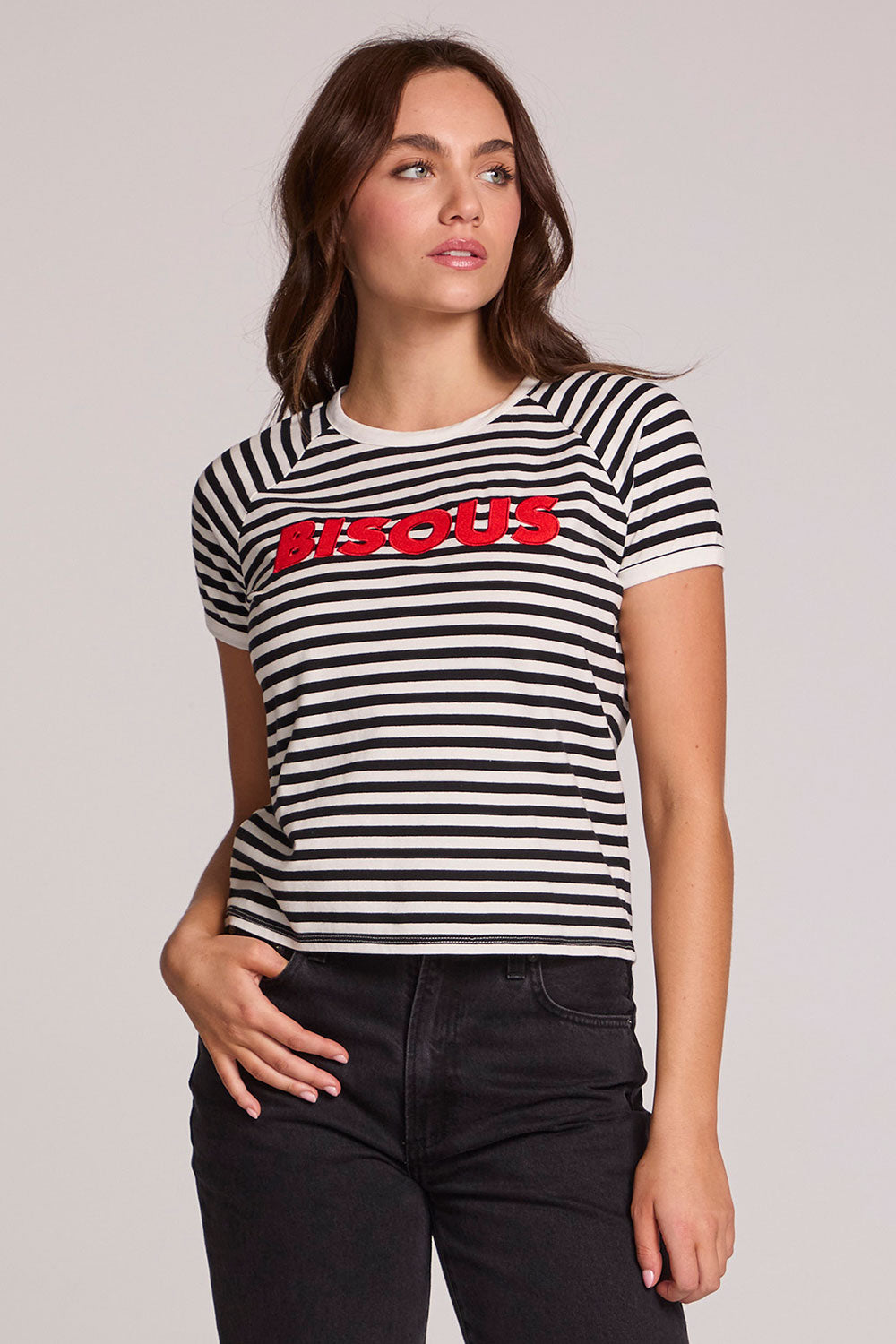 Front view of a woman wearing the Chaser Bisous Tee on a neutral background with black pants with hand on hip