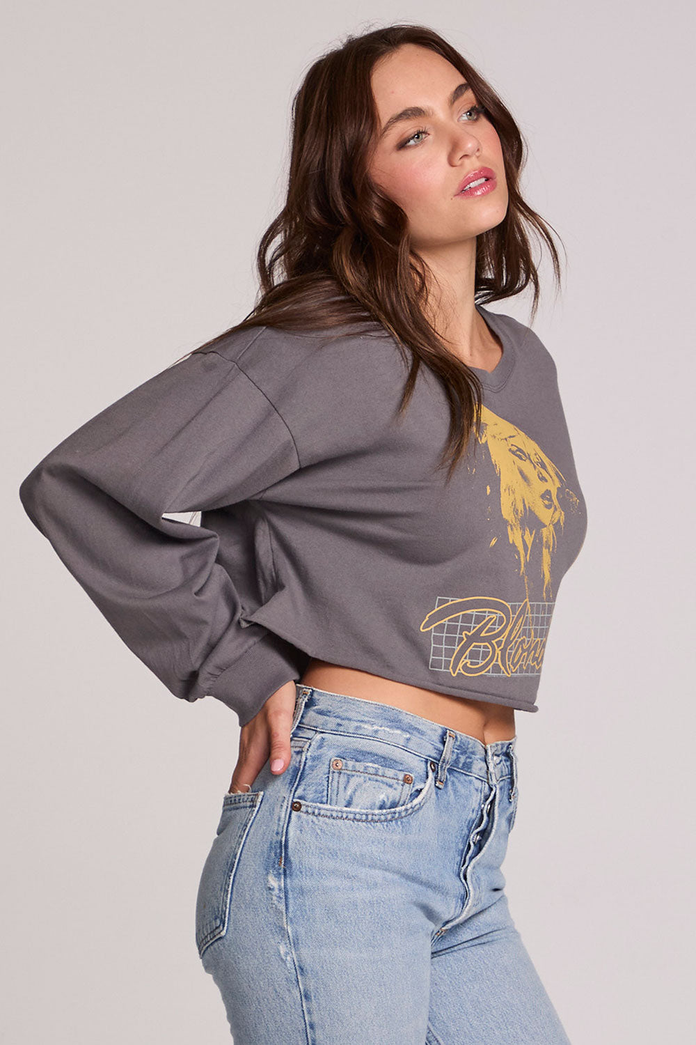 Side angle view of a woman wearing the Chaser Blondie Live Cropped Sweatshirt on a neutral background with hand in pocket