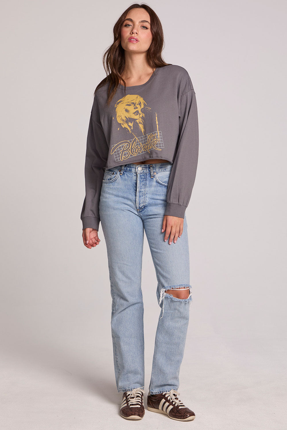 Full body view of a woman wearing the Chaser Blondie Live Cropped Sweatshirt on a neutral background with hands at sides and jeans