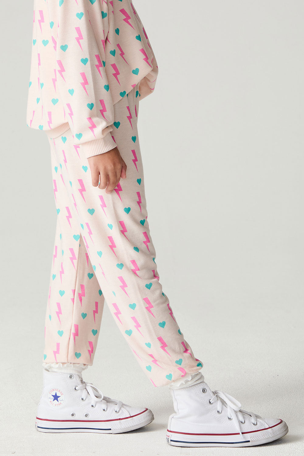 Side view of a girl wearing the Chaser Bolt Hearts Girls Jogger on a neutral background with long sleeve top