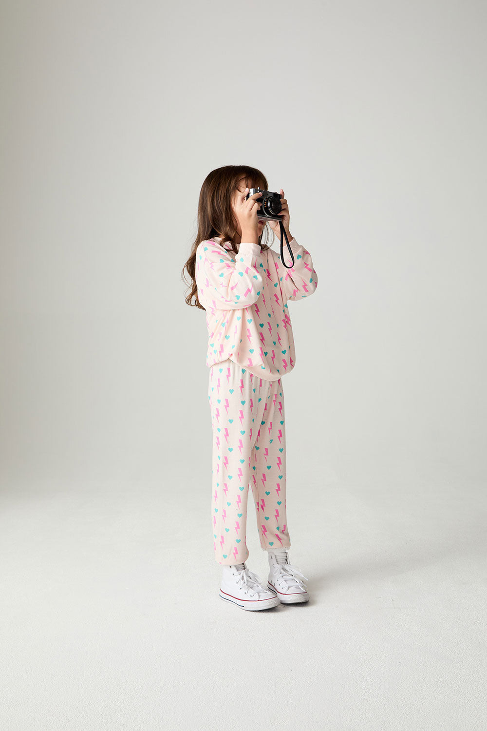 Front view of a girl wearing the Chaser Bolt Hearts Girls Jogger on a neutral background holding a camera