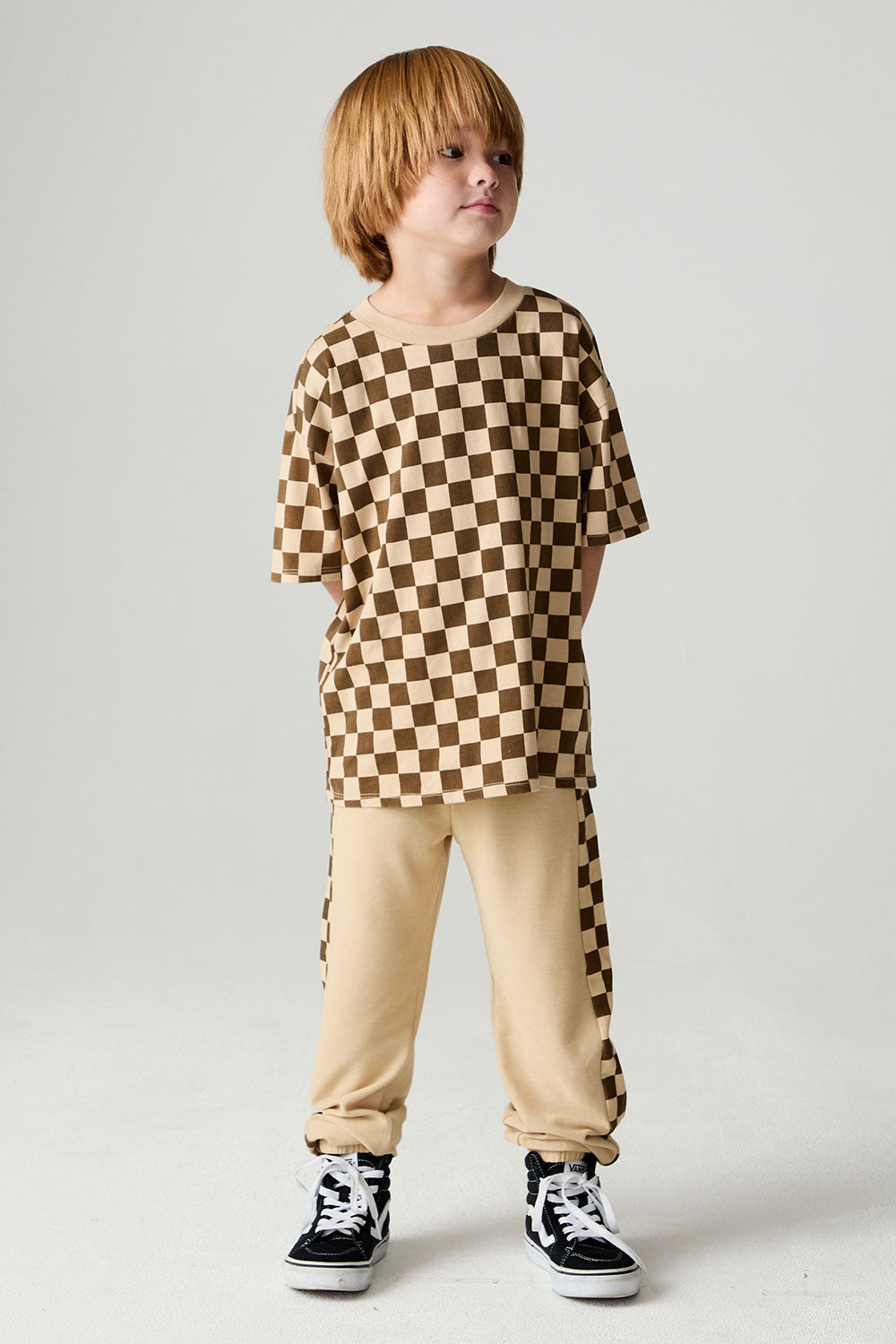 A full body front view of a boy wearing the Chaser Boys Solara Check Tee on a neutral background