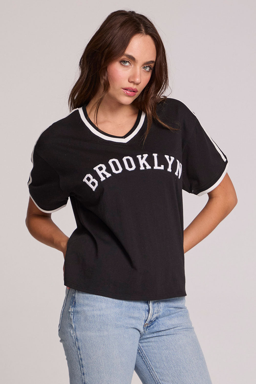 Front view of a woman wearing the Chaser Brooklyn Varsity Graphic Tee on a neutral background with hands on hips
