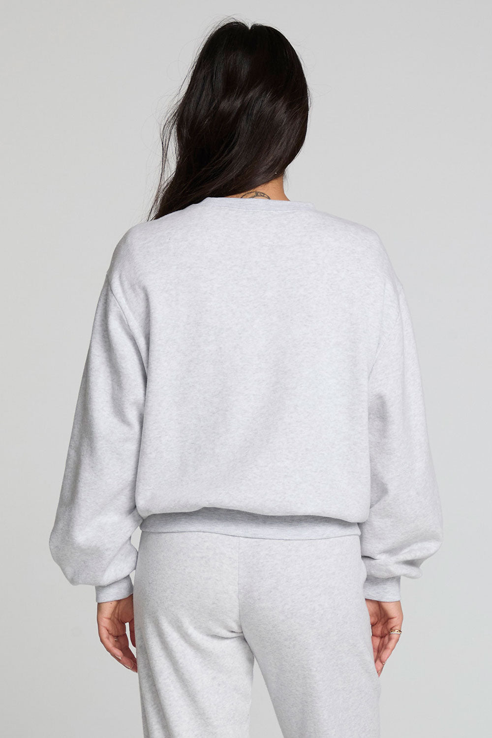 Back view of a woman wearing the Chaser  Cashbah Heather Grey Pullover and grey pants on a neutral background