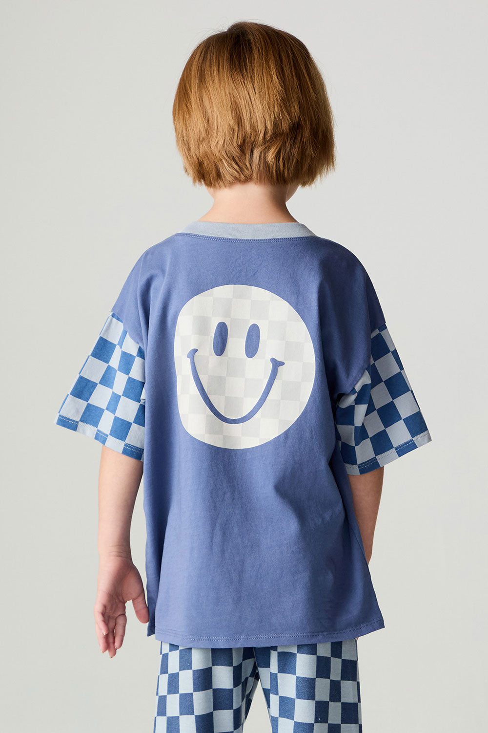 Back view of a boy wearing the Chaser Smileys Boys Tee on a neutral background with pants