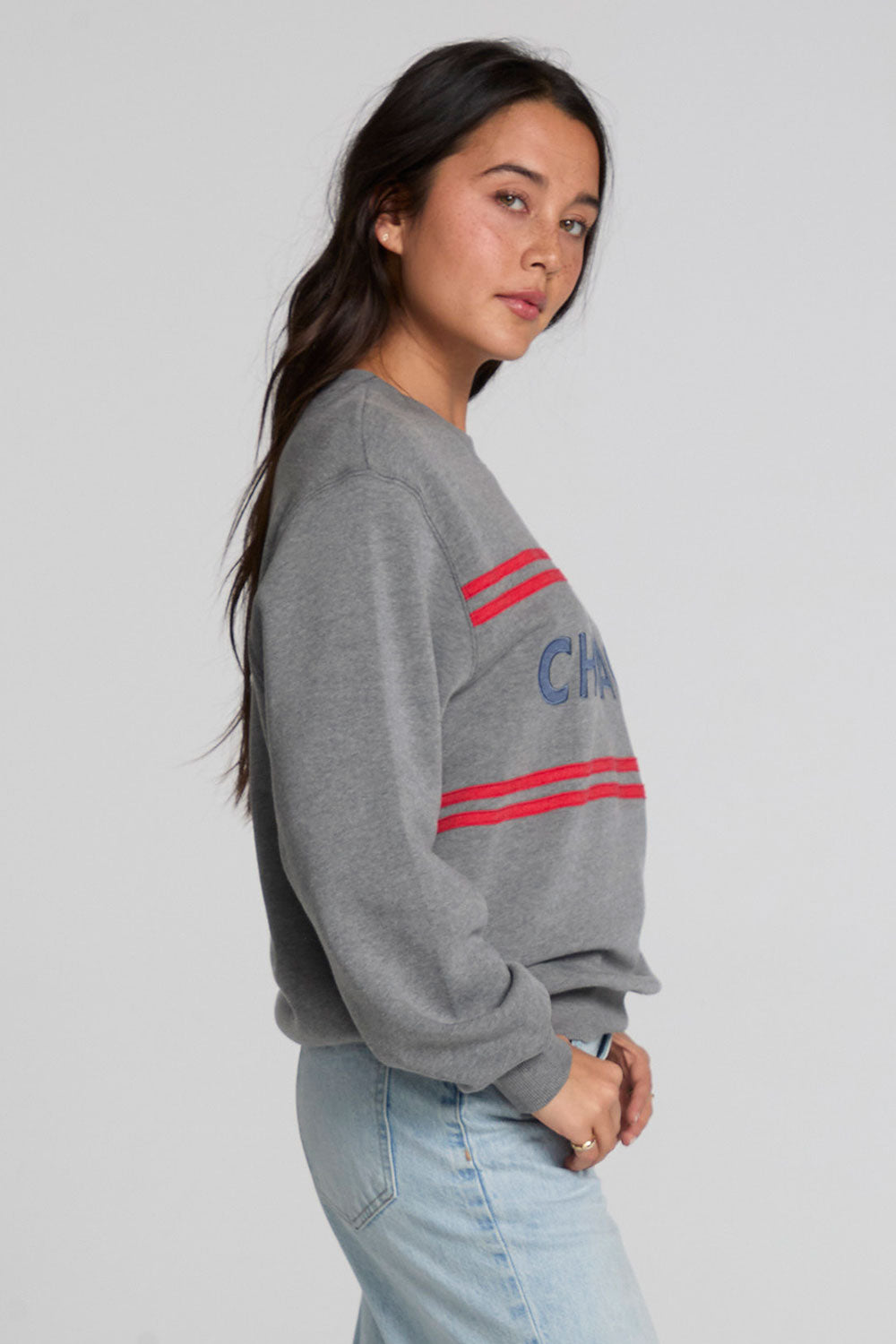 Side angle view of a woman wearing the Chaser Chicago Sweatshirt on a neutral background with hands on pickets