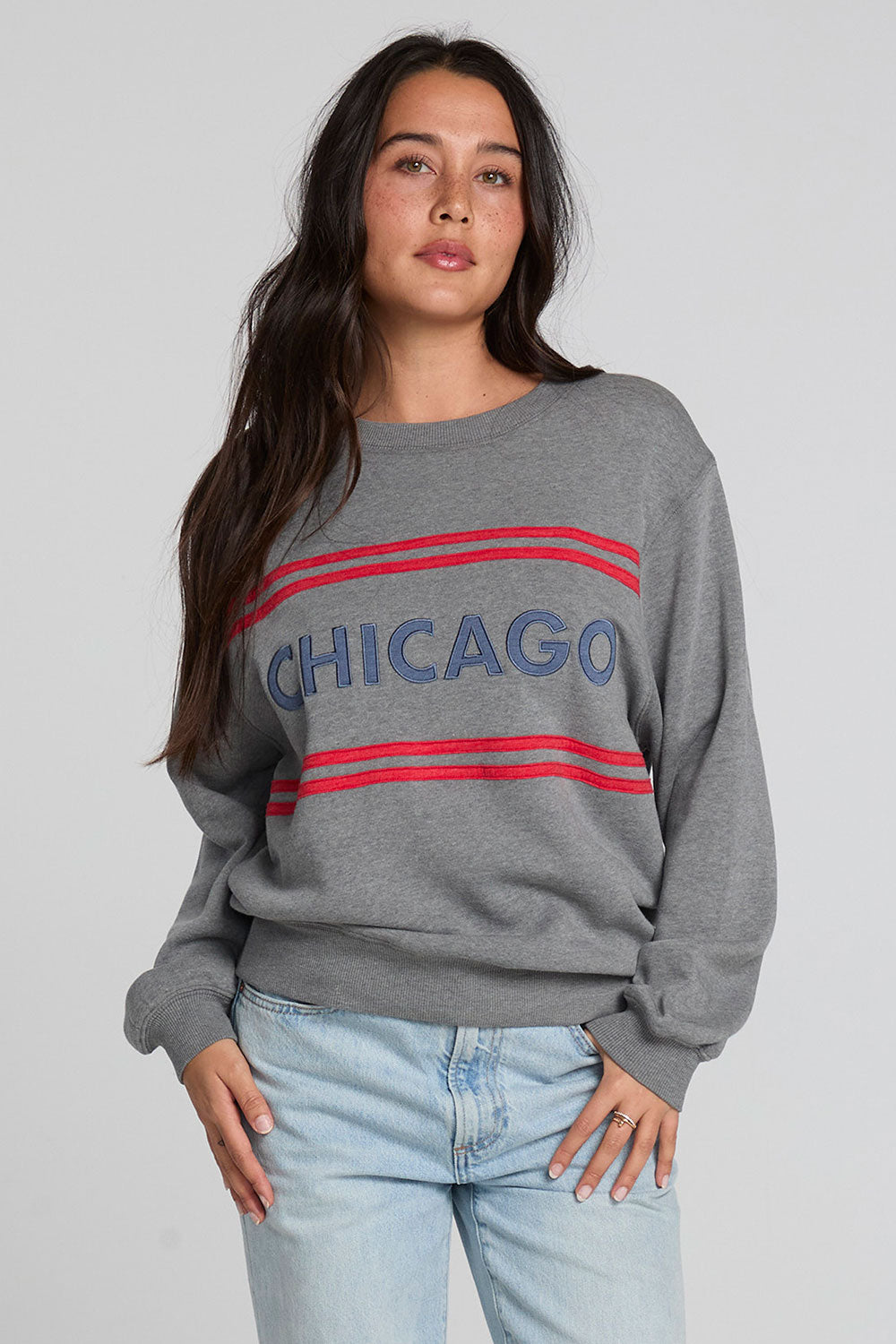 Front view of a woman wearing the Chaser Chicago Sweatshirt and jeans on a neutral background