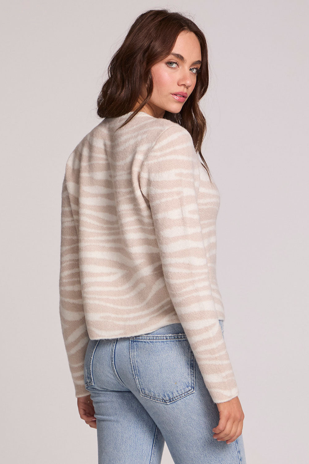 Back view of a woman wearing the Chaser   Zebra Dream Striped Cardigan on a neutral background with one hand in pocket