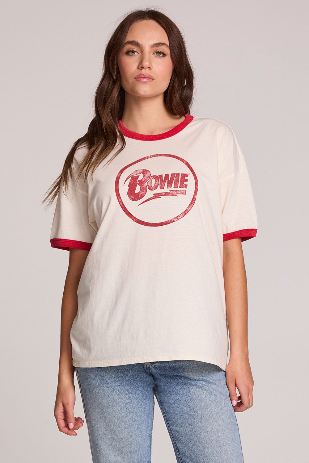 Front view of a woman wearing the Chaser David Bowie Bowie Bolt Tee on a neutral background with bluejeans and hands lowered
