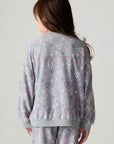 Back view of a girl wearing the Chaser Ditsy Hearts Girls Tee and pants on a neutral background