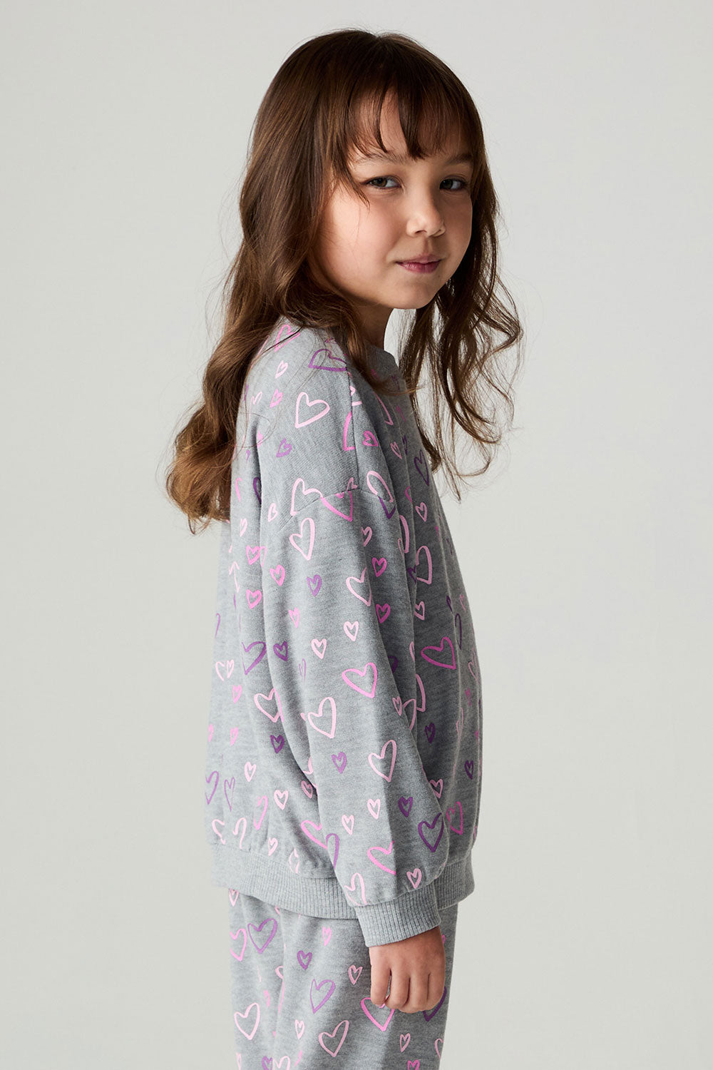Side view of a girl wearing the Chaser Ditsy Hearts Girls Tee and matching pants on a neutral background