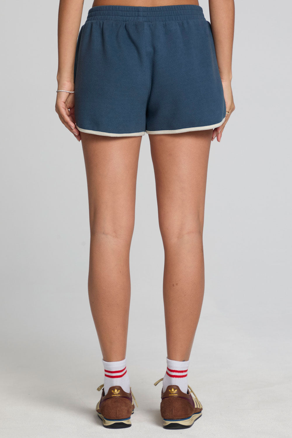 Back view of a woman wearing the Chaser  Eyla Dark Denim Shorts on a neutral background with brown sneakers and socks