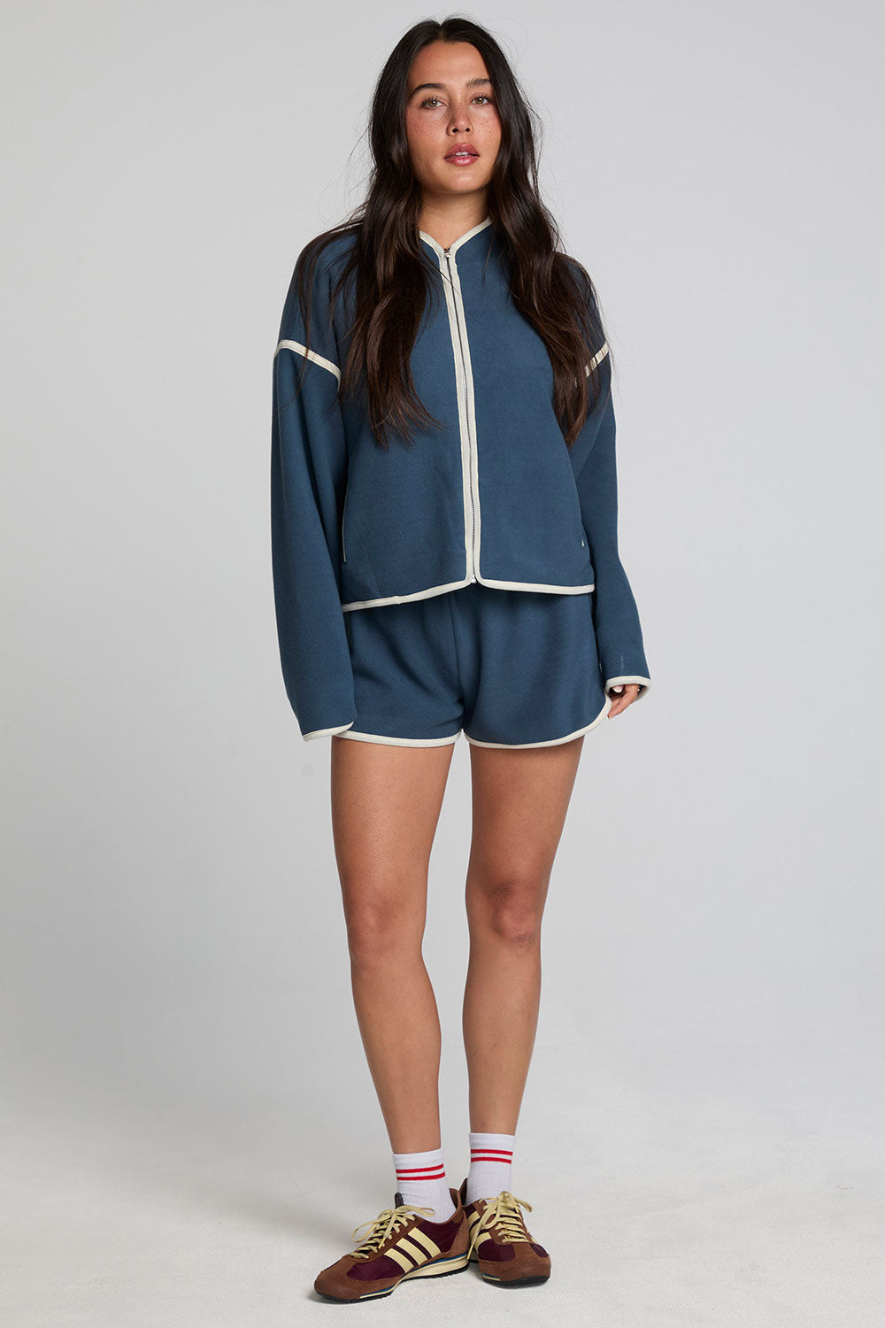 A full body front view of a woman wearing the Chaser  Eyla Dark Denim Shorts on a neutral background