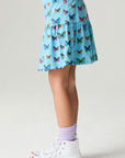 Side view of a girl wearing the Chaser Flutter Pop Girls Skirt on a neutral background with sneakers