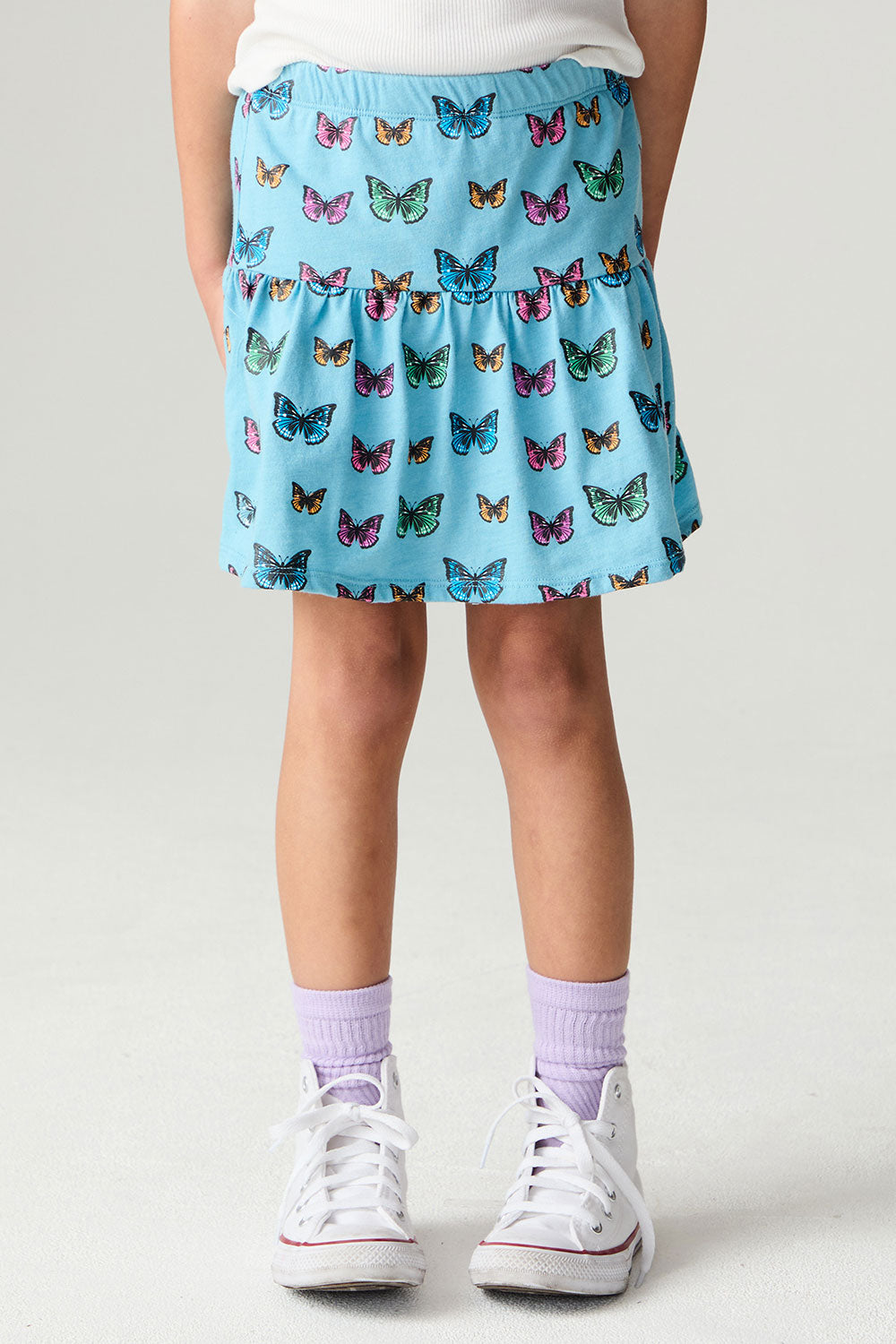 Front view of a girl wearing the Chaser Flutter Pop Girls Skirt on a neutral background with white sneakers and socks