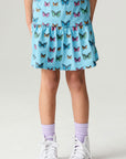 Front view of a girl wearing the Chaser Flutter Pop Girls Skirt on a neutral background with white sneakers and socks
