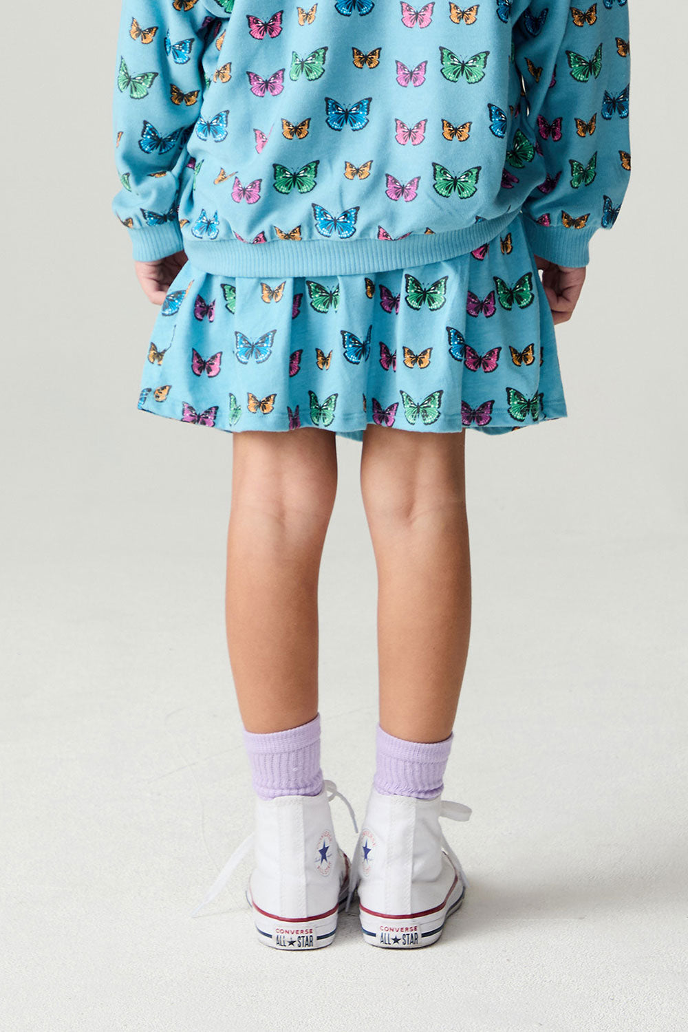 Back view of a girl wearing the Chaser Flutter Pop Girls Skirt on a neutral background