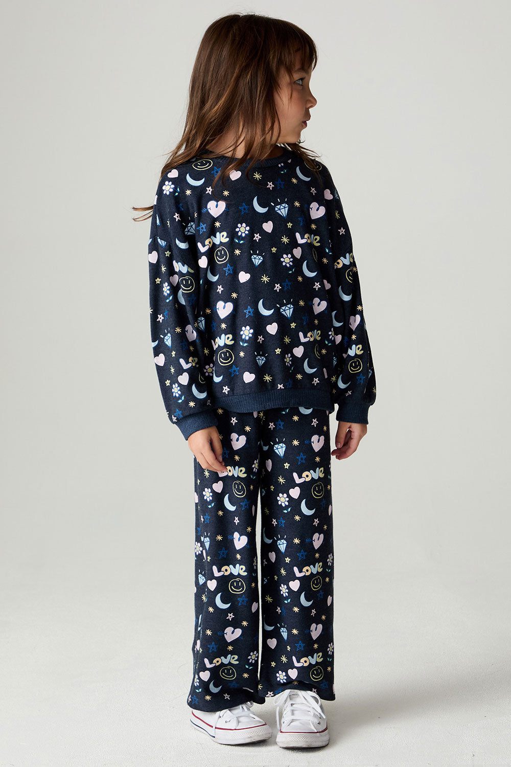 Full body front view of a girl wearing the Chaser Free Draw Girls Tee and pants on a neutral background looking to one side