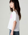 Side view of a girl wearing the Chaser Full Of Love Girls Tee on a neutral background with jeans and hands at sides