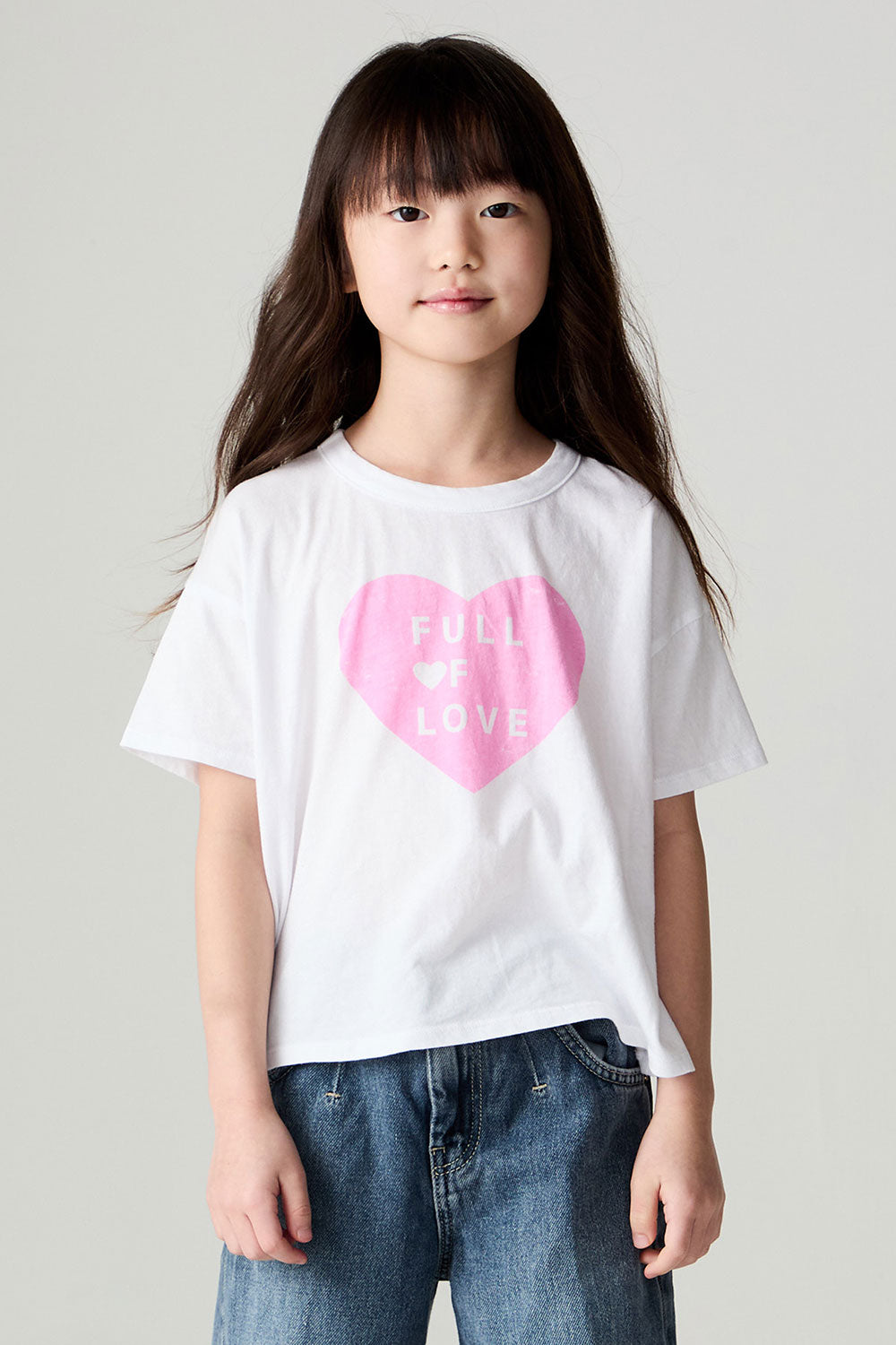 Front view of a girl wearing the Chaser Full Of Love Girls Tee on a neutral background with jeans and hands at sides of body
