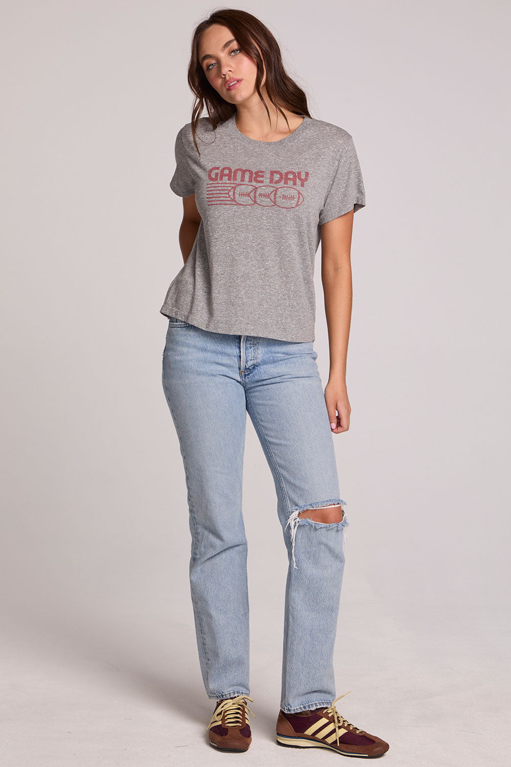 Full body front view of a woman wearing the Chaser Game Days Graphic Tee and jeans on a neutral background with arm behind her back