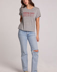 Full body front view of a woman wearing the Chaser Game Days Graphic Tee and jeans on a neutral background with arm behind her back
