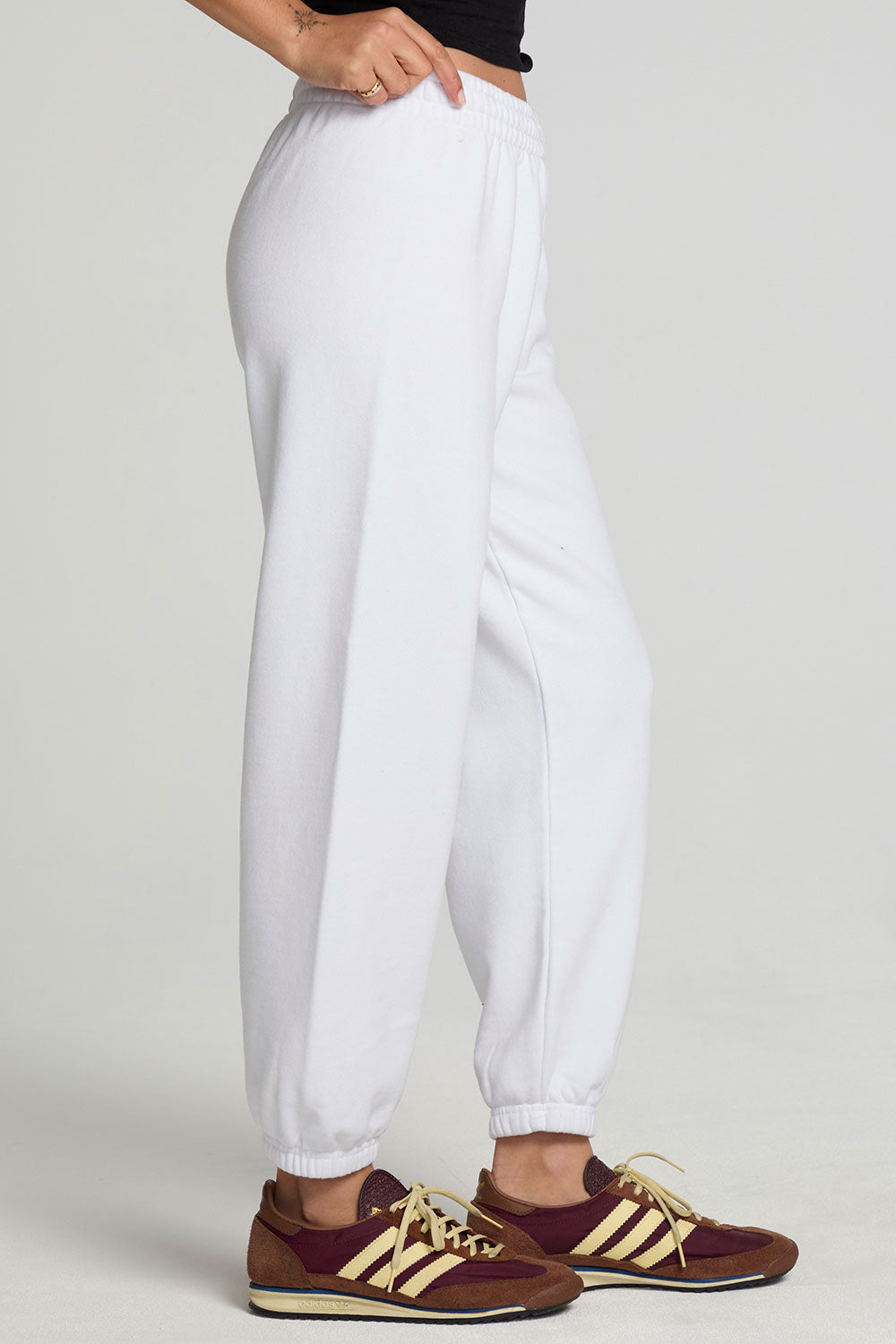 Side view of a woman wearing the Chaser  High Spirits Pants on a neutral background and arms in pockets